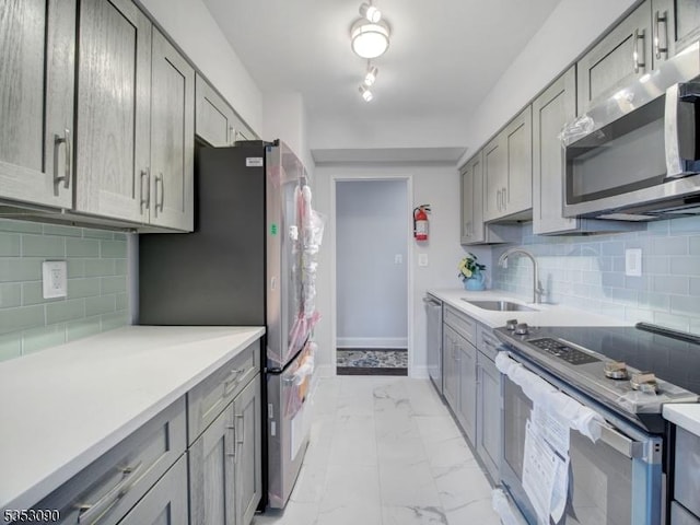 kitchen featuring decorative backsplash, stainless steel appliances, marble finish floor, a sink, and gray cabinetry