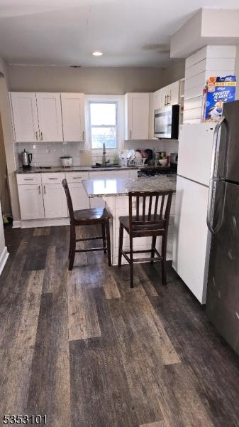 kitchen with white cabinets, a sink, dark wood finished floors, freestanding refrigerator, and stainless steel microwave