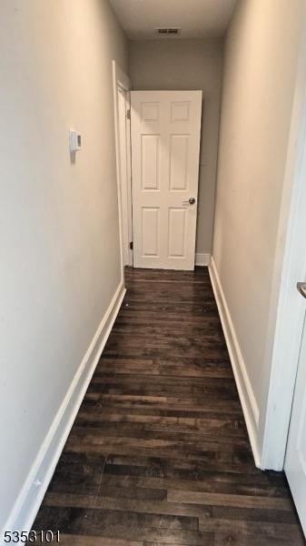 hall featuring baseboards, dark wood-style flooring, and visible vents