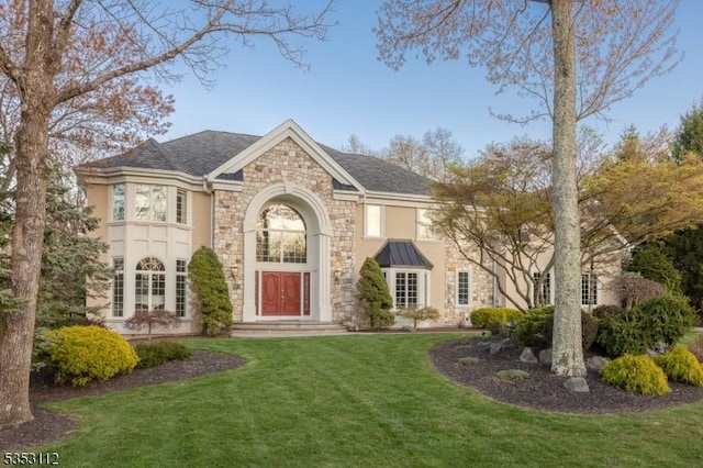 view of front of house with stucco siding, a front yard, and stone siding