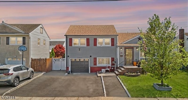tri-level home with a front lawn, fence, an attached garage, and aphalt driveway