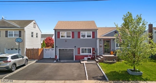 split level home featuring fence, aphalt driveway, a front lawn, and a garage