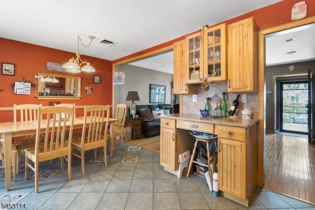 kitchen featuring glass insert cabinets, light tile patterned floors, a notable chandelier, tasteful backsplash, and hanging light fixtures