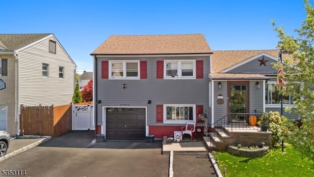 view of front of property with driveway, roof with shingles, an attached garage, and fence