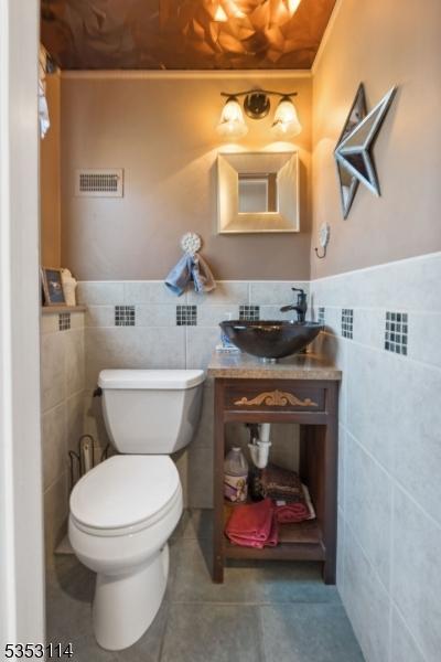 half bath featuring tile walls, visible vents, toilet, and tile patterned flooring