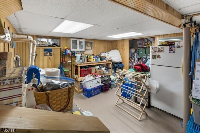 finished basement with wooden walls, a drop ceiling, and freestanding refrigerator