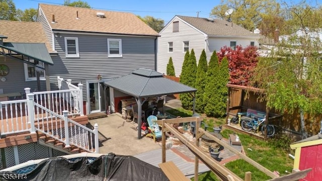 rear view of house featuring a deck, a shingled roof, and a patio area