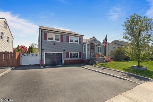 tri-level home featuring a front lawn, driveway, a garage, and fence