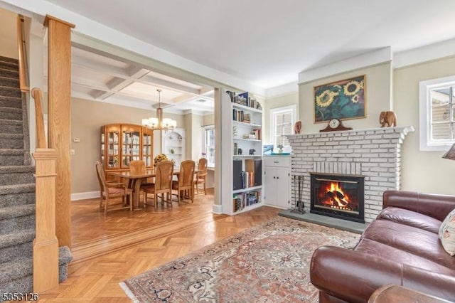living room featuring a brick fireplace, stairway, baseboards, a notable chandelier, and coffered ceiling
