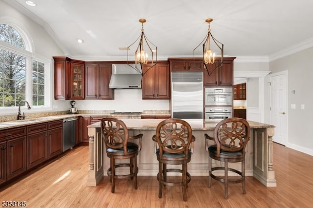 kitchen featuring wall chimney range hood, appliances with stainless steel finishes, a sink, a notable chandelier, and light wood-style flooring