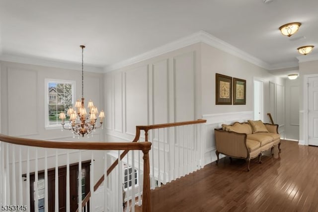 hall featuring crown molding, a decorative wall, a chandelier, hardwood / wood-style flooring, and an upstairs landing