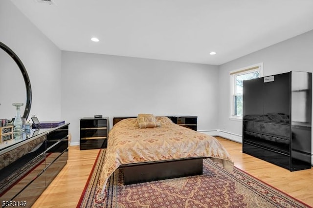bedroom with light wood-style floors, baseboards, and a baseboard heating unit