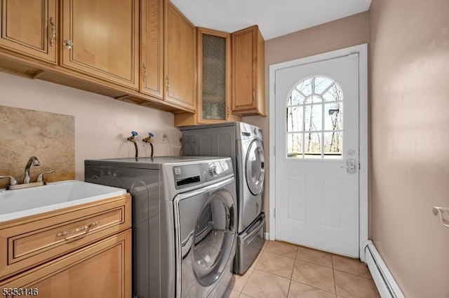 clothes washing area featuring washing machine and dryer, a baseboard heating unit, a sink, cabinet space, and light tile patterned floors