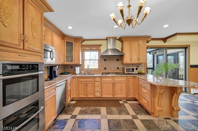 kitchen featuring wall chimney range hood, appliances with stainless steel finishes, a peninsula, a notable chandelier, and recessed lighting