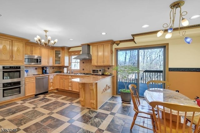 kitchen with decorative backsplash, wall chimney exhaust hood, appliances with stainless steel finishes, and a chandelier