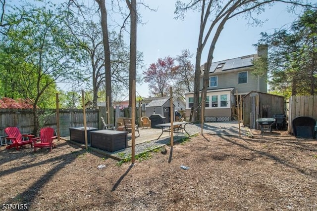 back of house with a patio area, roof mounted solar panels, an outdoor structure, a fenced backyard, and a shed