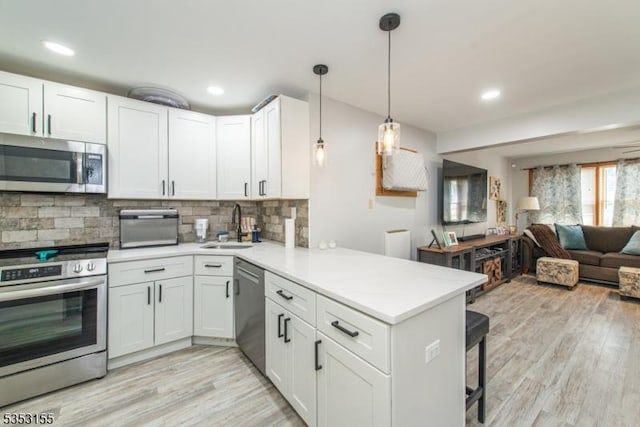 kitchen featuring appliances with stainless steel finishes, a sink, light wood-style floors, a peninsula, and open floor plan