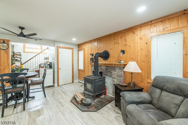 living area featuring a ceiling fan, a wood stove, wood walls, stairway, and light wood finished floors