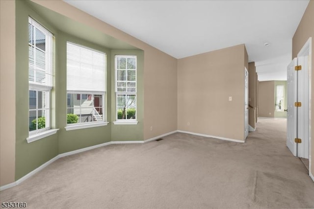 unfurnished room featuring baseboards, visible vents, light carpet, and a wealth of natural light