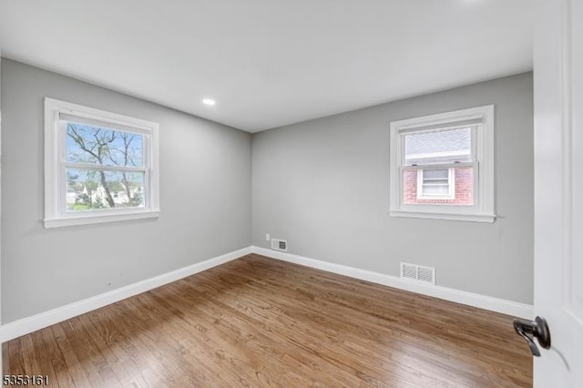 empty room featuring visible vents, a healthy amount of sunlight, and wood finished floors