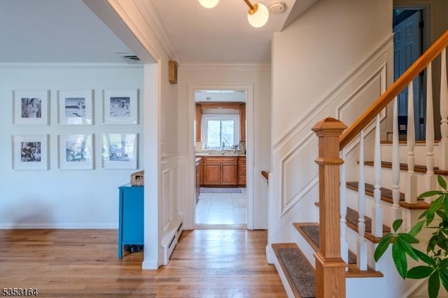 corridor featuring crown molding, a baseboard radiator, light wood-style floors, a decorative wall, and stairs