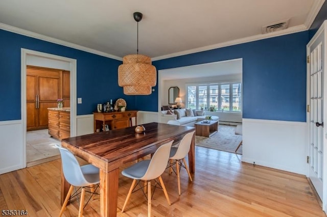dining space featuring visible vents, baseboard heating, wainscoting, light wood-style floors, and ornamental molding