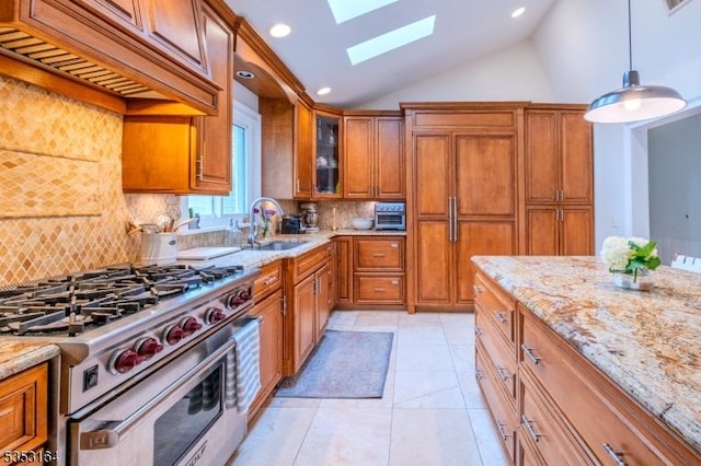 kitchen featuring vaulted ceiling with skylight, brown cabinets, a sink, light stone counters, and high end stainless steel range
