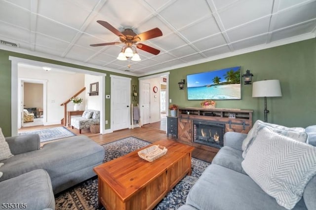 living area featuring visible vents, wood finished floors, a ceiling fan, and a glass covered fireplace