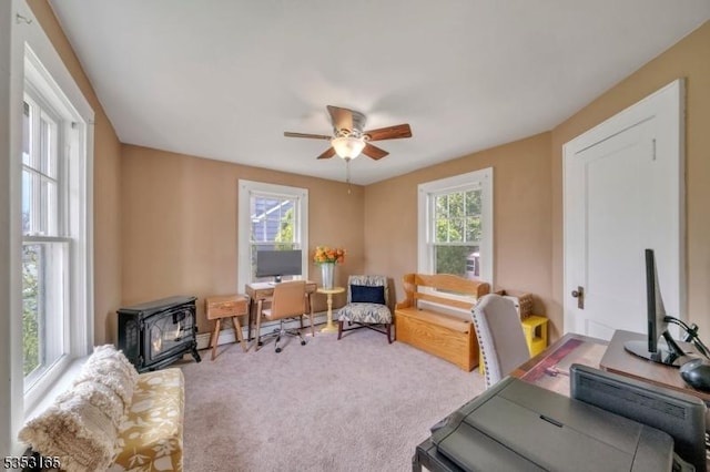 carpeted office space with ceiling fan, plenty of natural light, and a wood stove