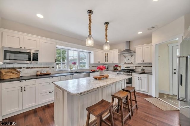 kitchen with decorative backsplash, visible vents, wall chimney range hood, white cabinets, and appliances with stainless steel finishes
