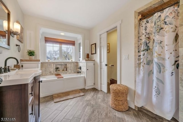 full bath with wood finished floors, vanity, a garden tub, and a shower with curtain