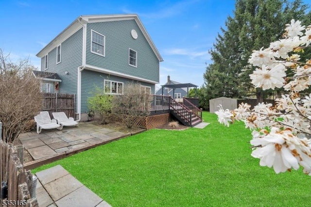 back of house featuring a patio, a wooden deck, a lawn, a shed, and fence