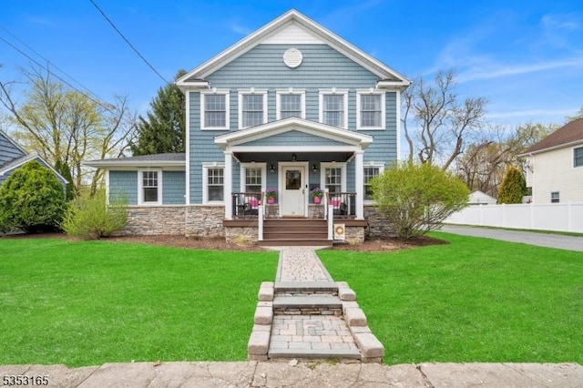 traditional-style house with a porch, a front yard, stone siding, and fence