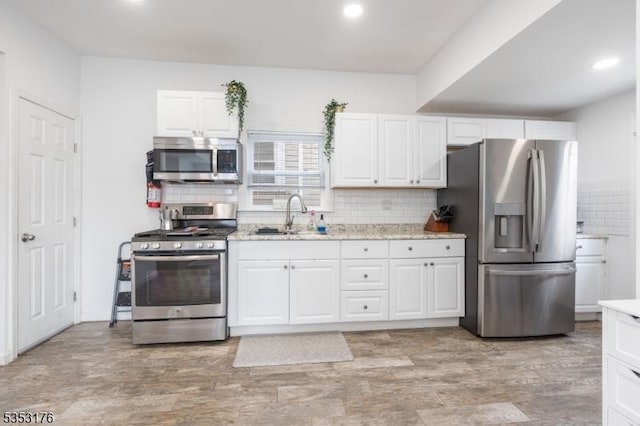 kitchen with recessed lighting, white cabinets, a sink, appliances with stainless steel finishes, and backsplash