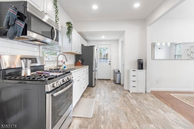 kitchen featuring white cabinets, a sink, light wood-style floors, stainless steel appliances, and tasteful backsplash