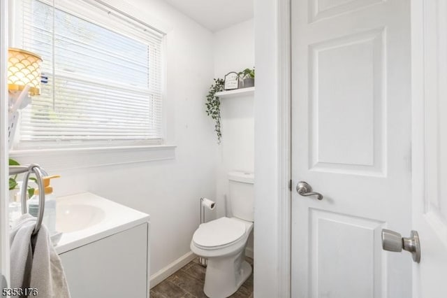 half bathroom featuring toilet, baseboards, wood finished floors, and vanity