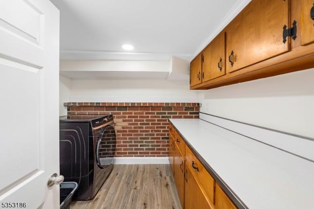 interior space featuring independent washer and dryer, brick wall, light wood-type flooring, cabinet space, and baseboards