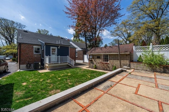 back of property featuring fence, central air condition unit, brick siding, an outbuilding, and a lawn