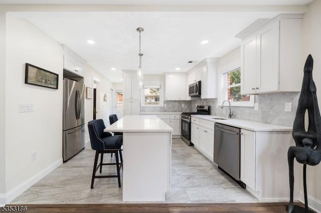 kitchen with a breakfast bar area, a kitchen island, a sink, light countertops, and stainless steel appliances