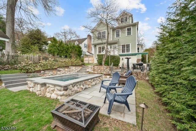 rear view of house with an outdoor hot tub, fence, a patio area, and a fire pit