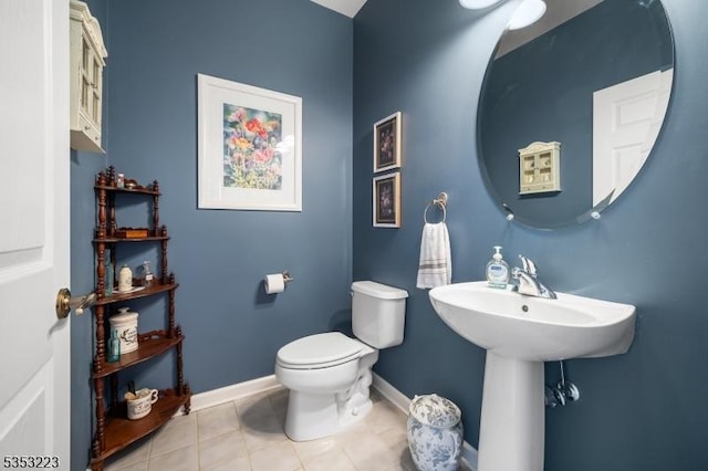 half bath featuring toilet, tile patterned floors, a sink, and baseboards