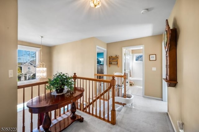 hall with carpet flooring, a notable chandelier, an upstairs landing, and baseboards