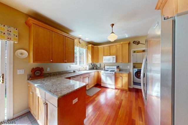 kitchen with a peninsula, white appliances, washer / clothes dryer, a sink, and light wood-style flooring