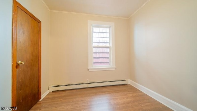 empty room featuring crown molding, baseboard heating, wood finished floors, and baseboards