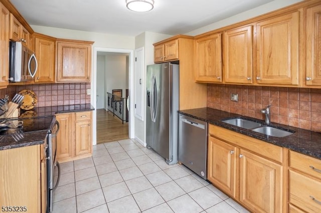 kitchen featuring a sink, stainless steel appliances, light tile patterned flooring, dark stone countertops, and tasteful backsplash