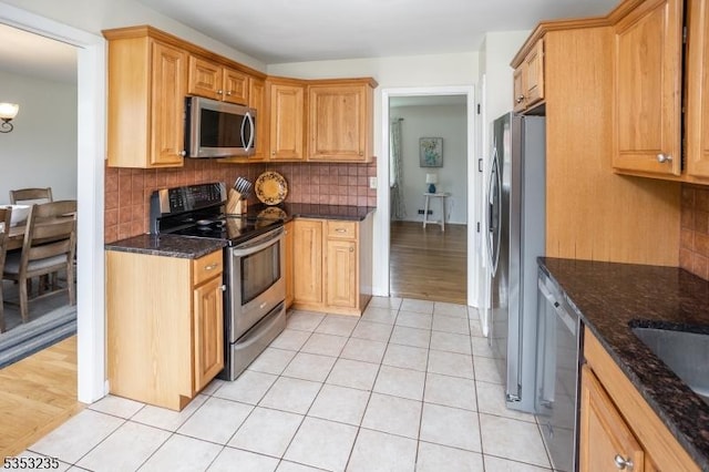 kitchen featuring dark stone counters, tasteful backsplash, stainless steel appliances, and light tile patterned floors