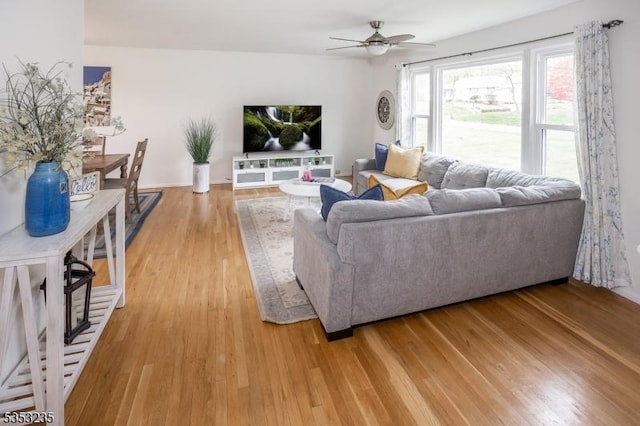 living room featuring baseboards, a ceiling fan, and light wood-style flooring
