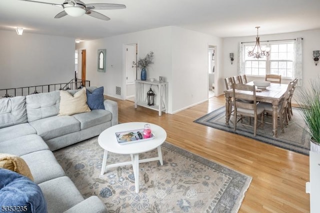 living room with baseboards, wood finished floors, and ceiling fan with notable chandelier