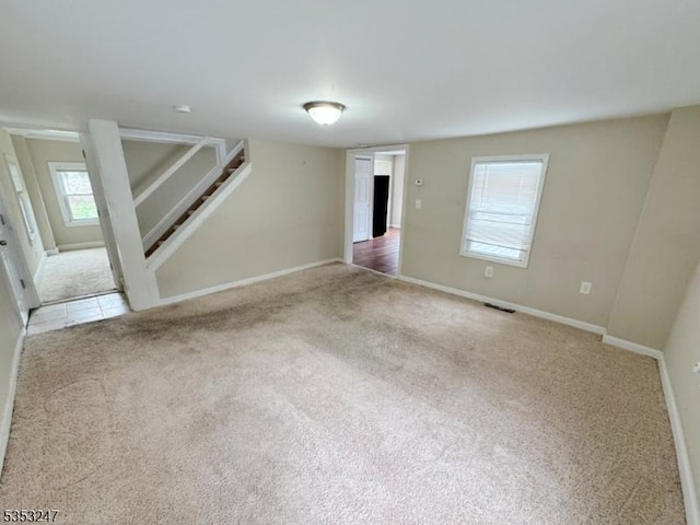unfurnished living room featuring baseboards, visible vents, stairs, and carpet flooring
