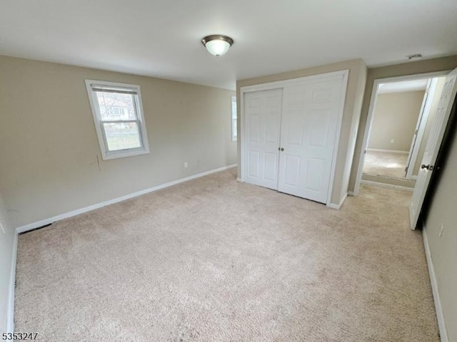 unfurnished bedroom featuring light colored carpet, baseboards, and a closet